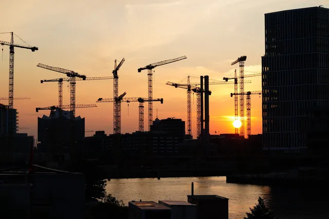 Saulėlydis virš miesto statybų zonos – profesionalūs įrankiai ir technika nuomai statybų projektams.